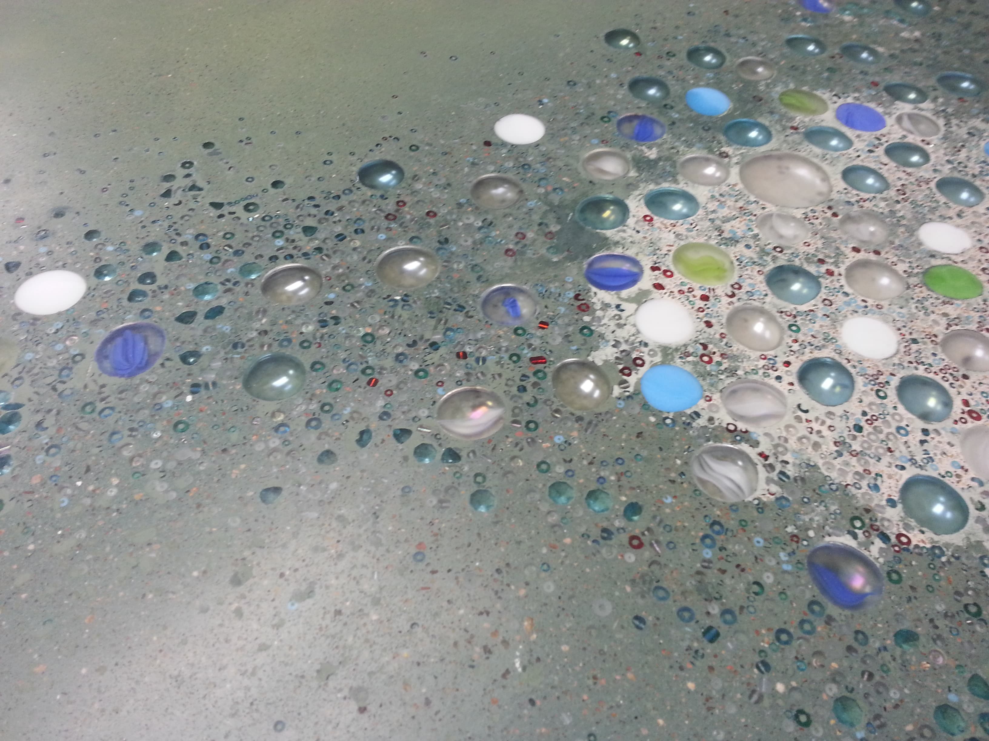 Close-up of sage concrete with embedded glass, beads and sequins
