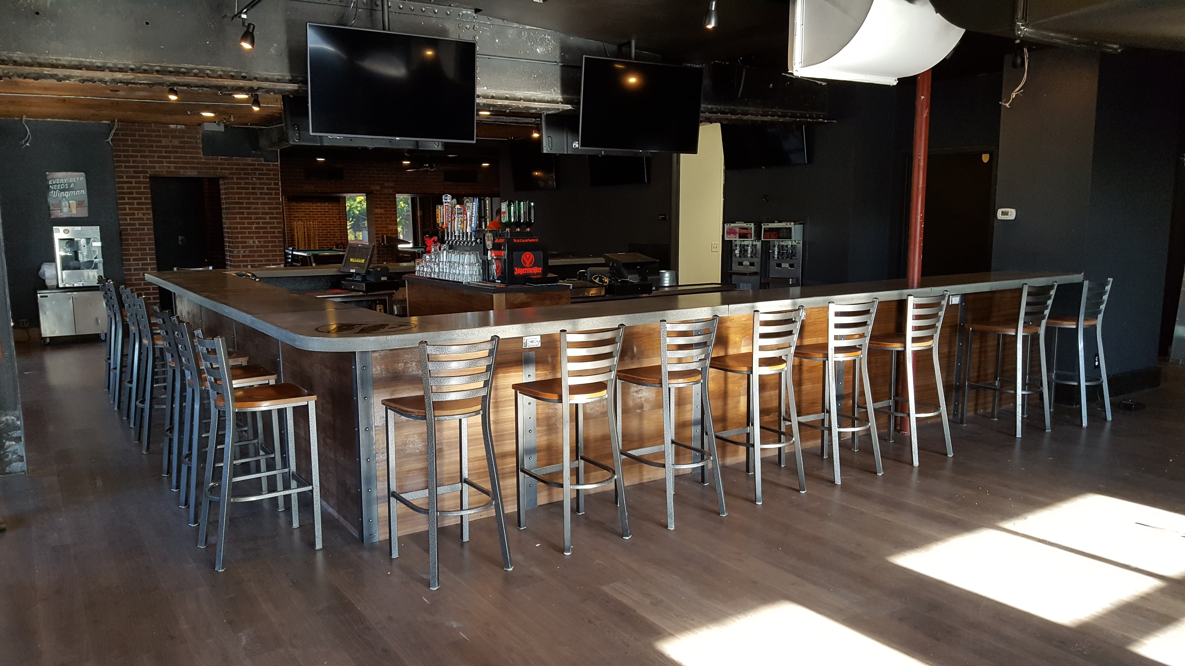 L-shaped concrete bar with a row of stools in a brick-walled taproom